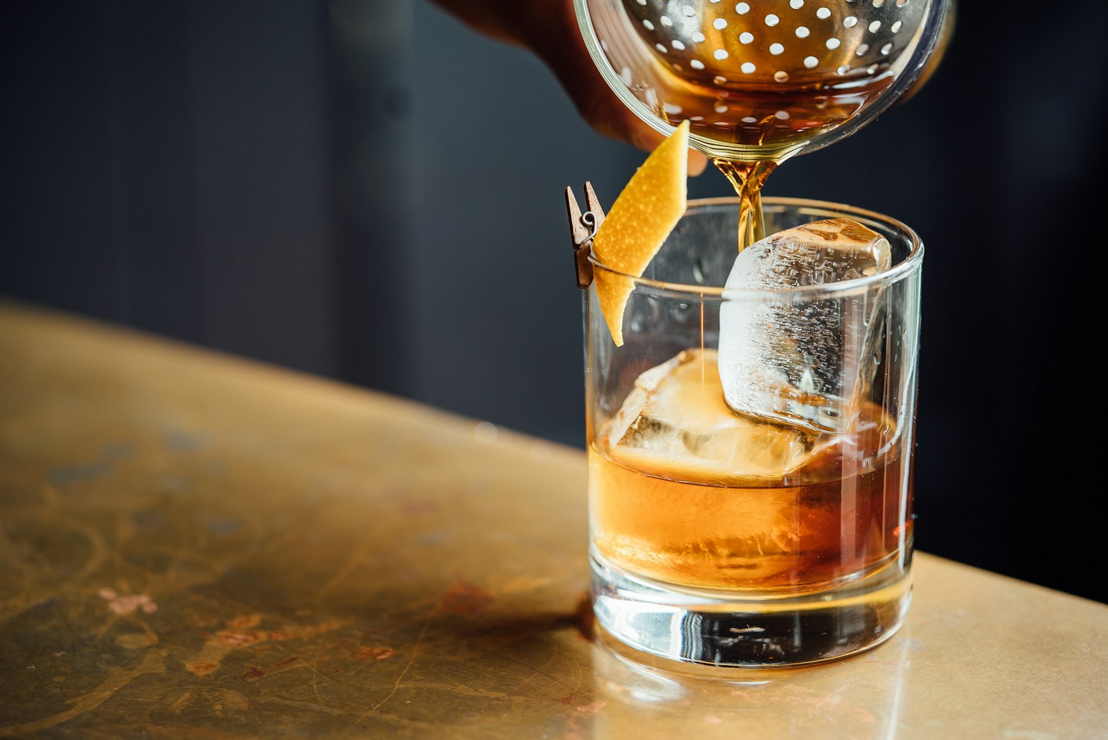 An amber cocktail being poured over ice with a citrus garnish